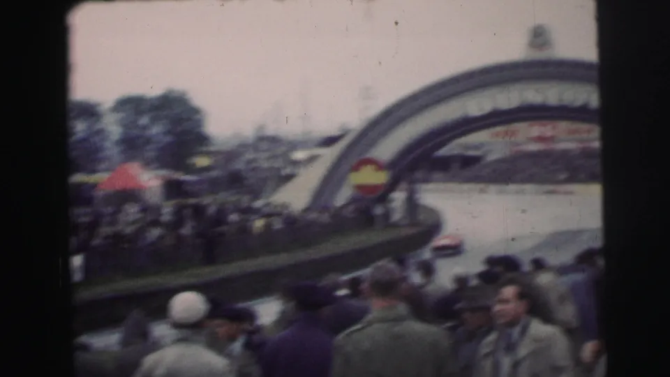 1954 Le Mans home-movie view of spectators watching a race car pass beneath or near the Dunlop arch.