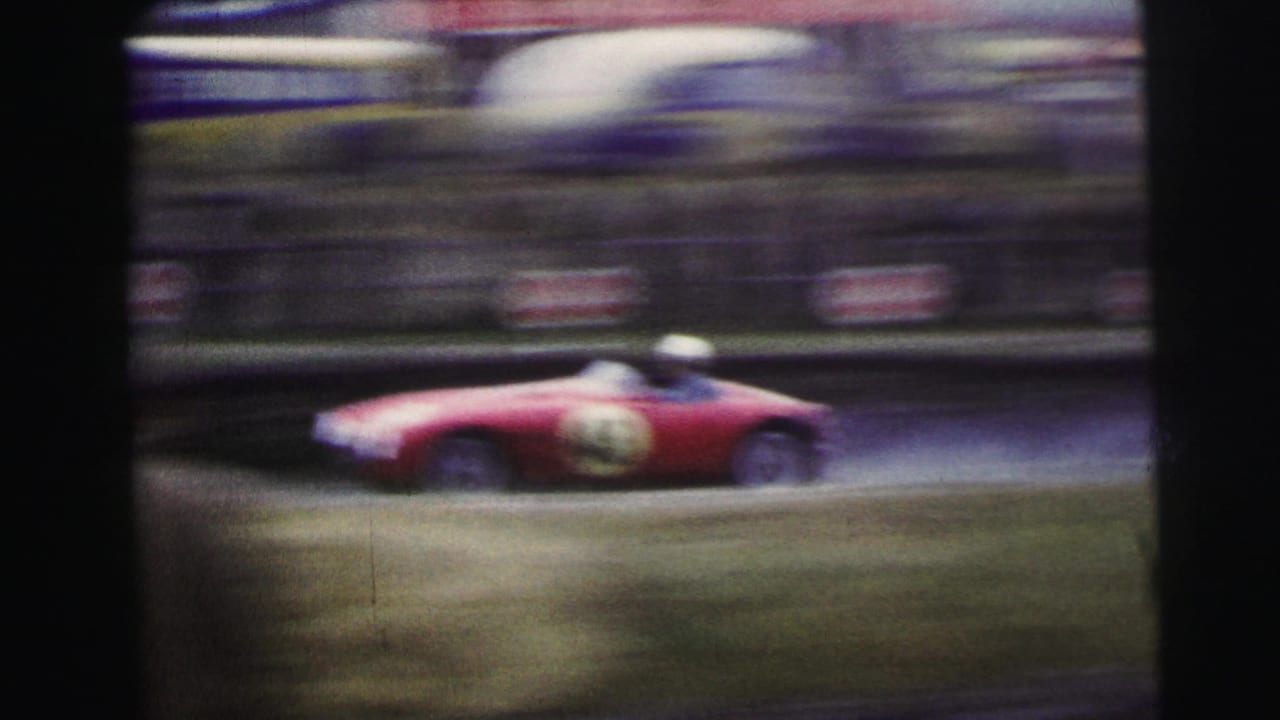Red vintage racing car speeds past at Le Mans with spectators blurred in the background.