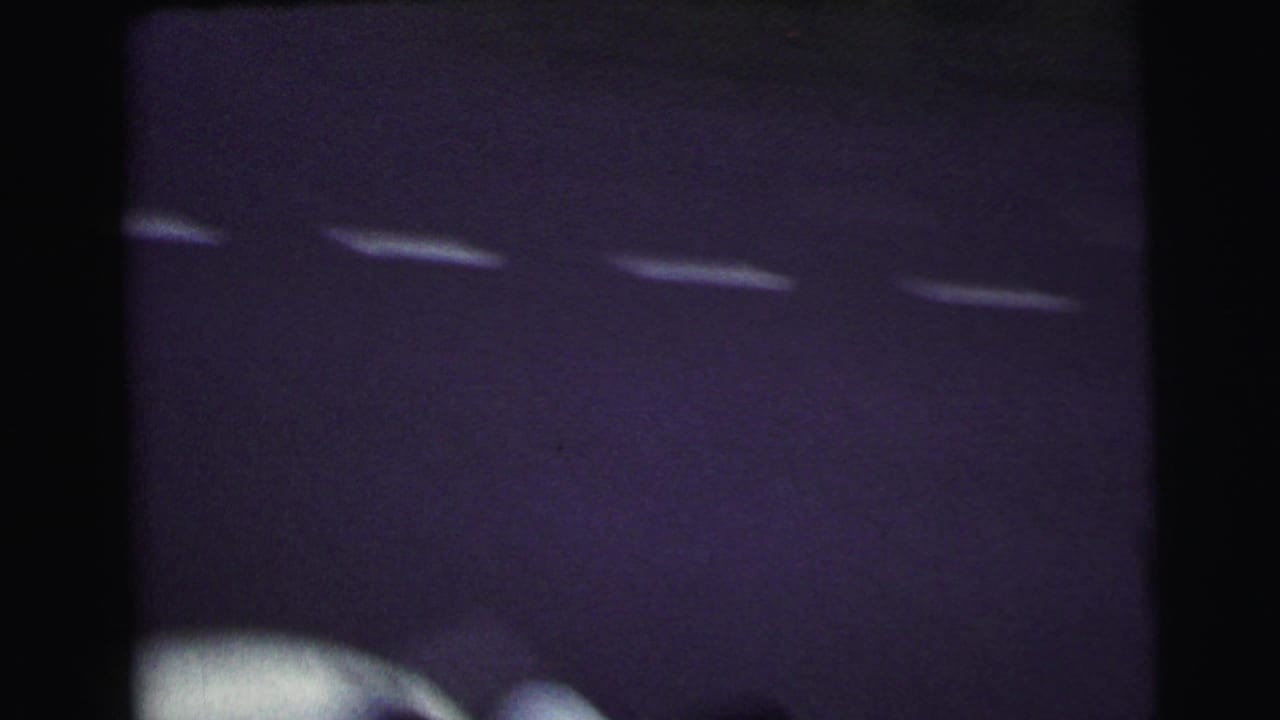Soft 8mm frame from the Le Mans clip showing dark pavement, white markings, and a blurred vehicle edge.
