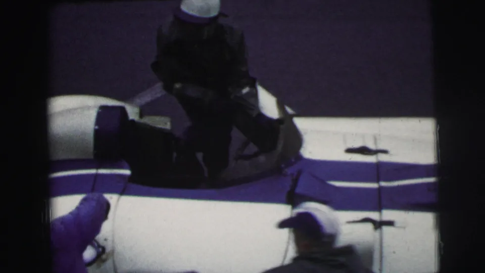 Le Mans, France 1954 frame showing a dark-clad person in an open blue-and-white race car with spectators or crew nearby.