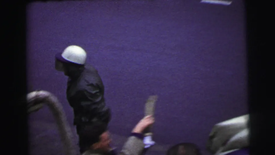 Le Mans, France 1954 home-movie frame showing a man in a white cap or helmet walking near spectators and vehicle edges.