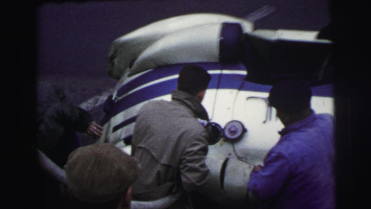 Men stand beside the rear section of a white-and-blue race car.