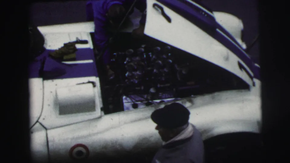 Overhead 1954 Le Mans frame showing a capped man beside a white race car with its hood raised and engine exposed.