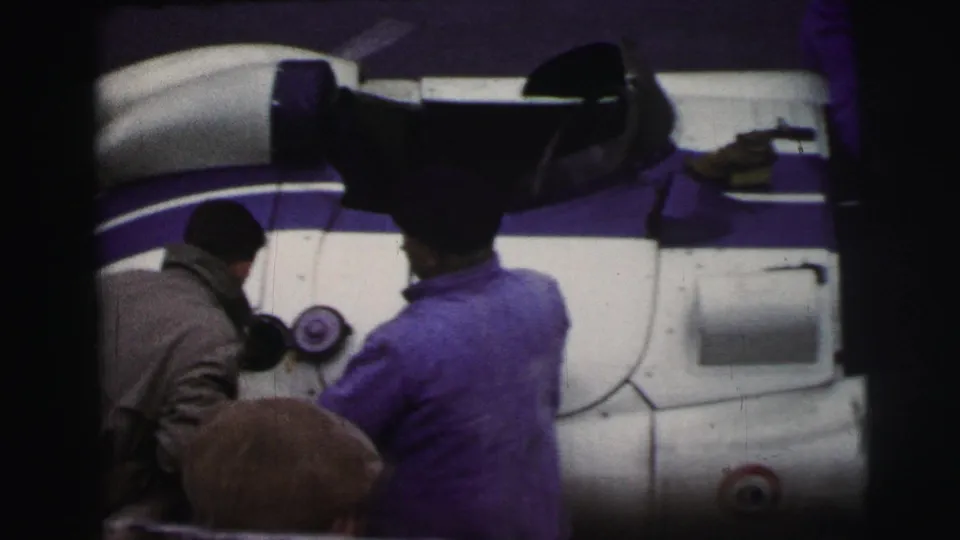 At Le Mans, France in 1954, mechanics in workwear attend to a white and purple race car beside the track.