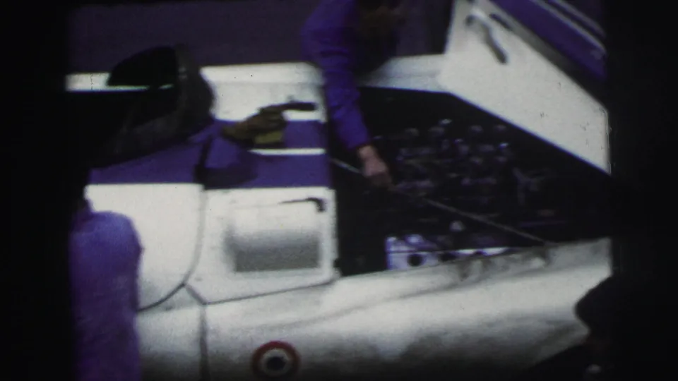 The open rear of the white and purple race car is visible as pit crew activity continues at the 1954 Le Mans setting.
