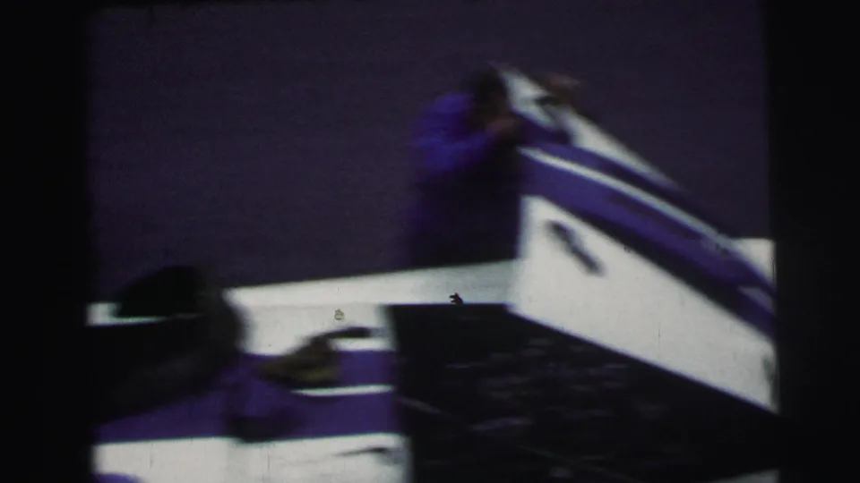 A mechanic moves quickly near the rear of the race car, captured with blur and handheld 8mm framing.