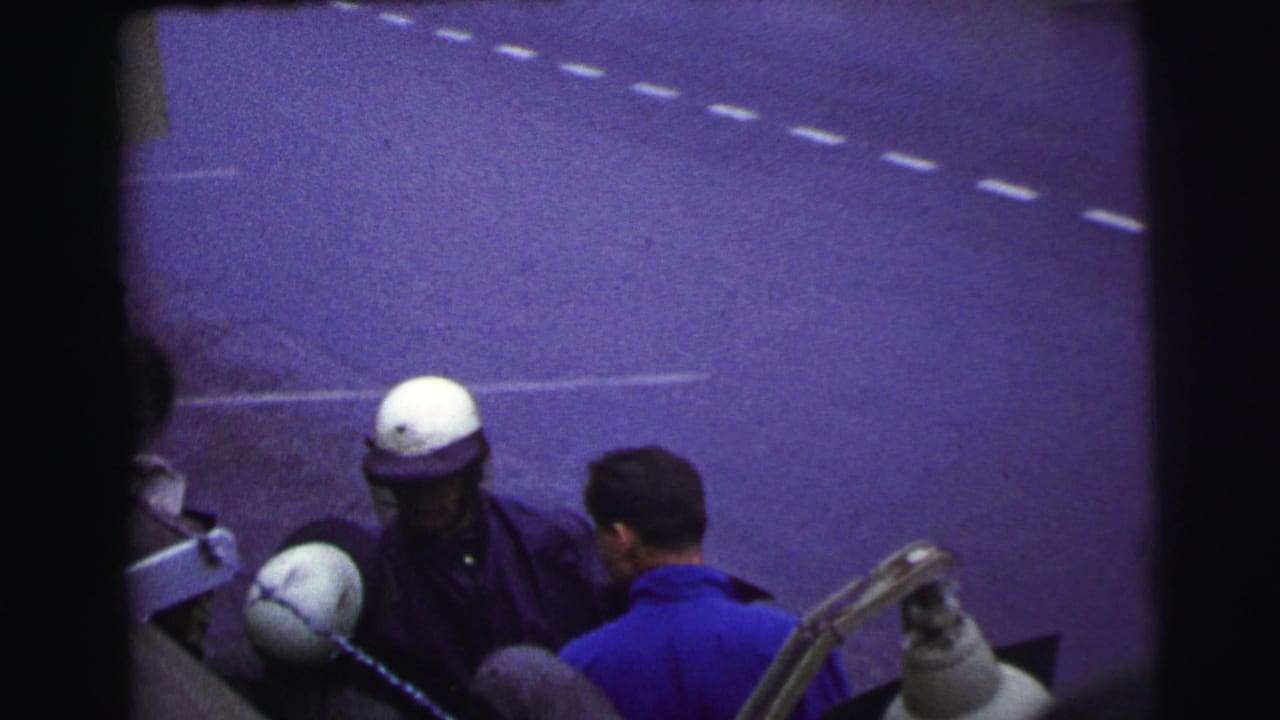 Helmeted race official near a man in a blue shirt at the edge of a roadway.