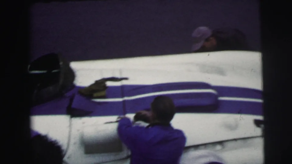A blue-and-white race car body at 1954 Le Mans is seen from above as crew members work around the pit area.
