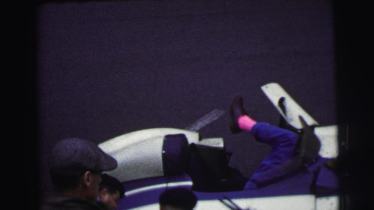 Mechanic leans into a white and blue race car while spectators watch nearby.