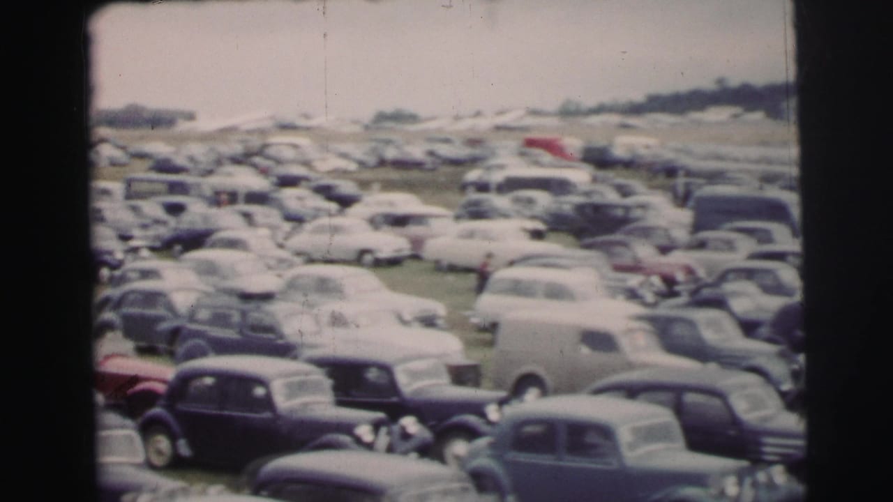 1954 Le Mans parking field with rows of mid-century cars seen from a soft, handheld 8mm viewpoint.