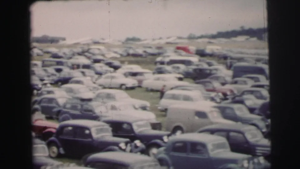 1954 Le Mans parking field with rows of mid-century cars seen from a soft, handheld 8mm viewpoint.
