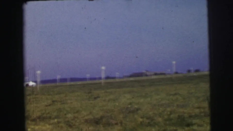 A wide field view in the Le Mans home movie shows grass, white posts, distant low structures, and a purple-blue sky.