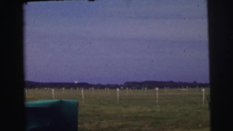 The final frame looks across an open field near Le Mans, with white posts, a distant tree line, and a dusky sky.