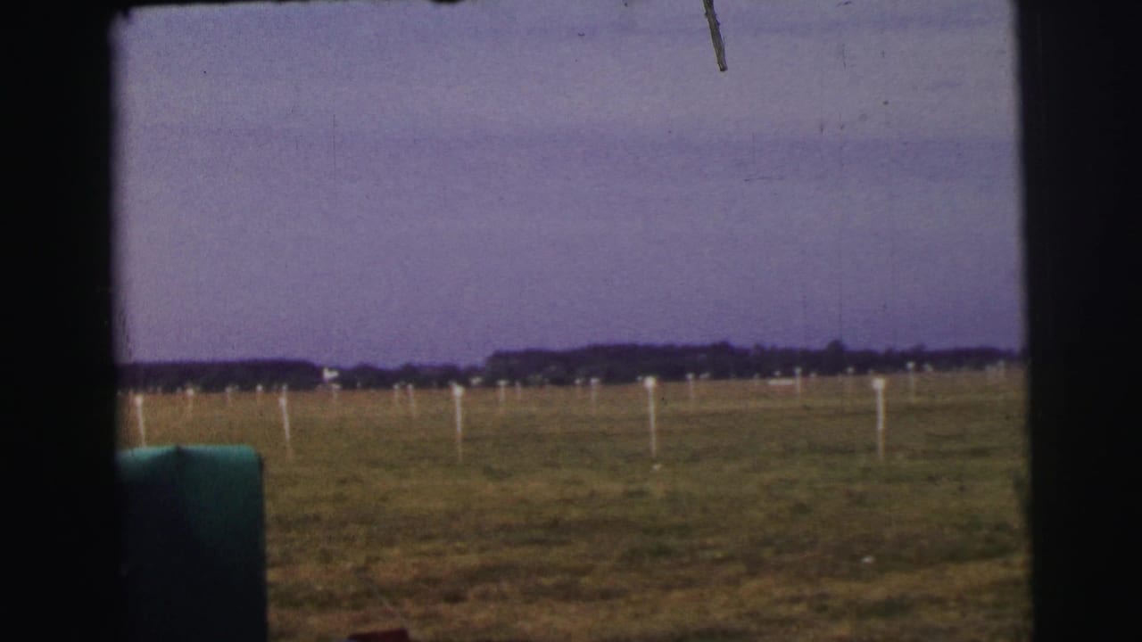 Le Mans airfield landscape with white field markers, open grass, distant trees, and dark vehicle framing in the foreground.