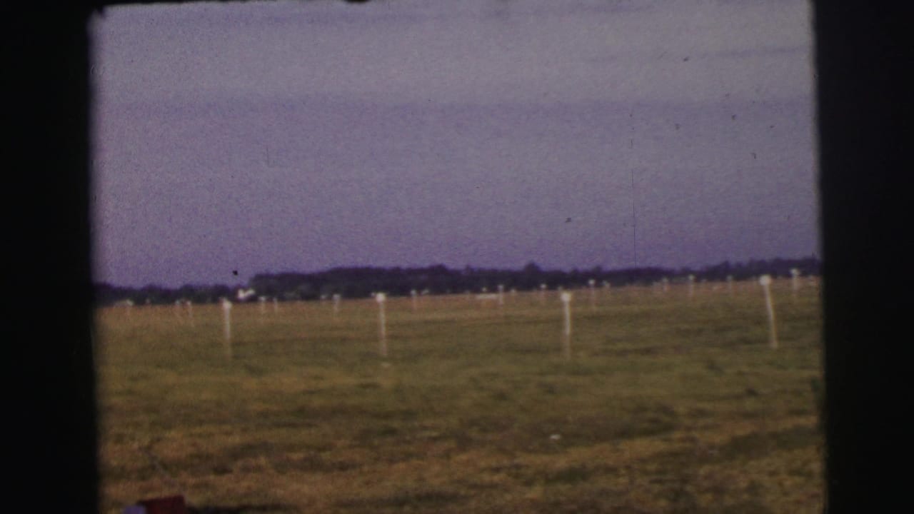 1954 Le Mans airfield view with grass, white marker posts, distant treeline, and no aircraft clearly centered in the frame.
