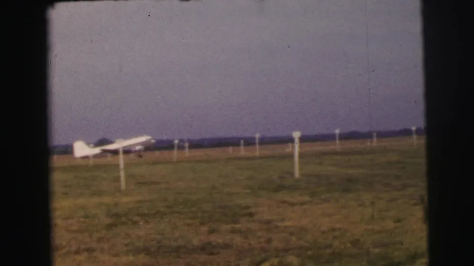A 1954 home-movie view in Le Mans shows the small plane still parked on grass behind foreground marker posts.