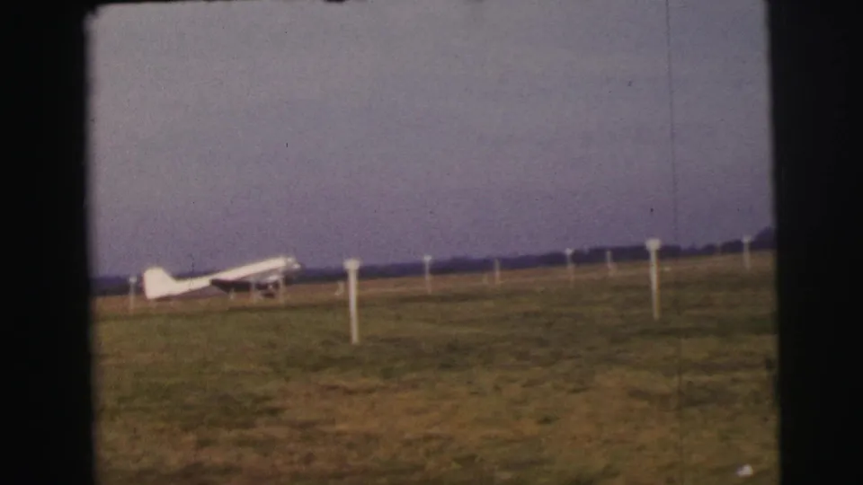 Final 1954 Le Mans frame holds on the small white aircraft, grassy airfield, marker poles, and subdued sky.