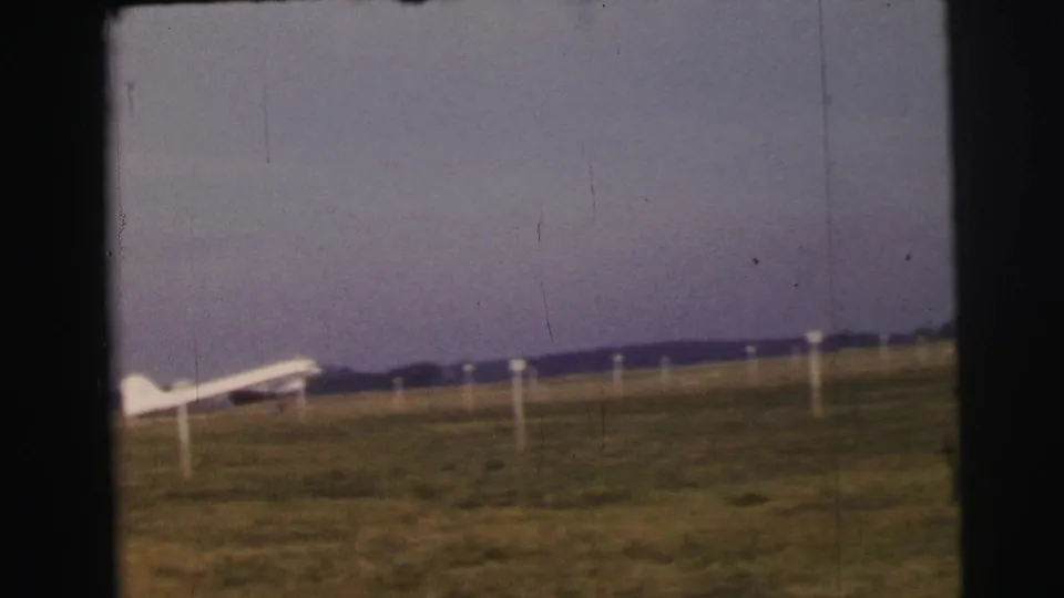Le Mans airfield frame with a small white airplane near the left edge and white posts across the grass.