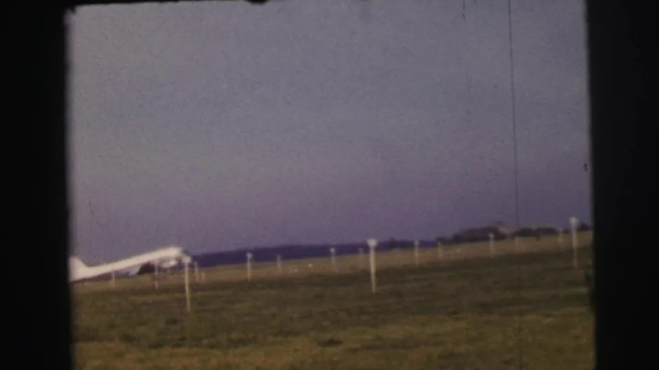Final 1954 Le Mans frame showing the small aircraft at the left of a grassy airfield with perimeter posts.