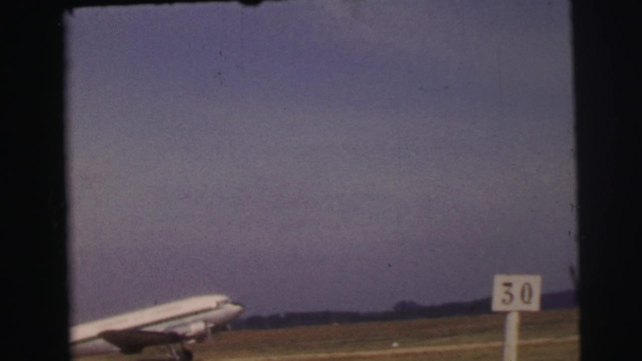 1954 Le Mans 8mm frame of a large passenger plane taxiing across a grassy airfield near a visible 50 runway marker.