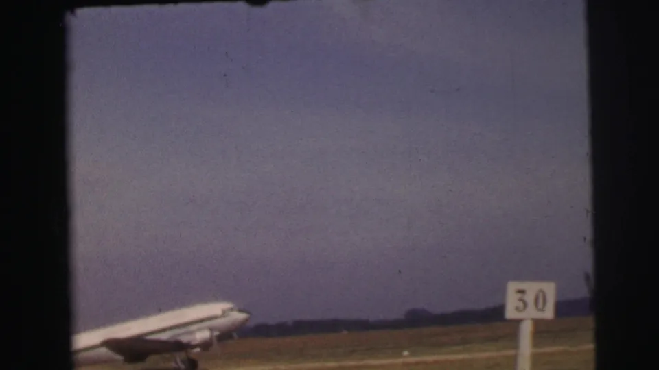 1954 Le Mans 8mm frame of a large passenger plane taxiing across a grassy airfield near a visible 50 runway marker.