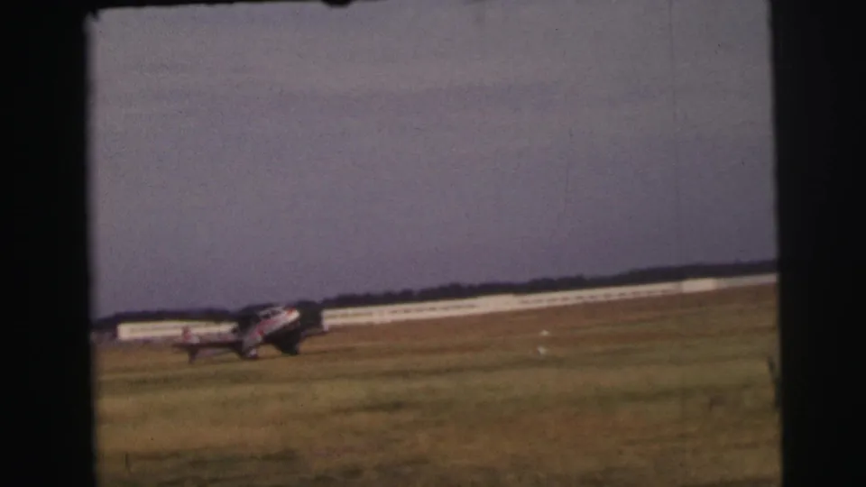 Final frame shows the small propeller aircraft on the Le Mans grass airfield with a long white building in the background.