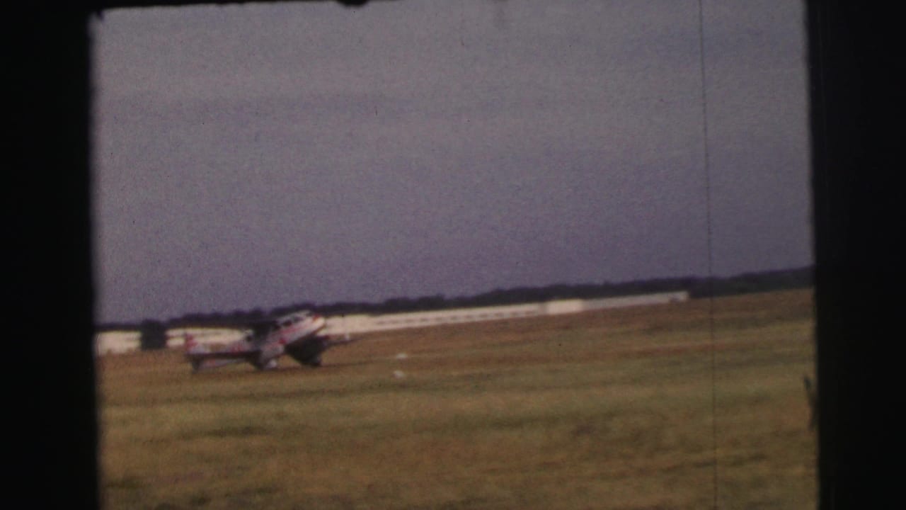 Small propeller airplane on a grassy airfield beneath a muted sky.