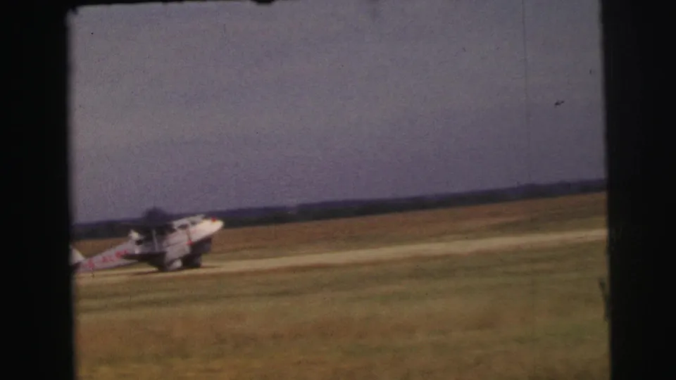 The small aircraft continues taxiing across the grass runway in a soft, grainy 1954 Le Mans aviation shot.