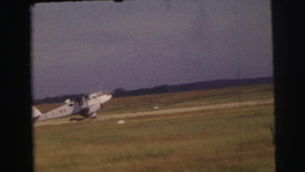 A small white propeller aircraft with red markings taxis on a grass runway in Le Mans, France, according to the 1954 clip metadata.