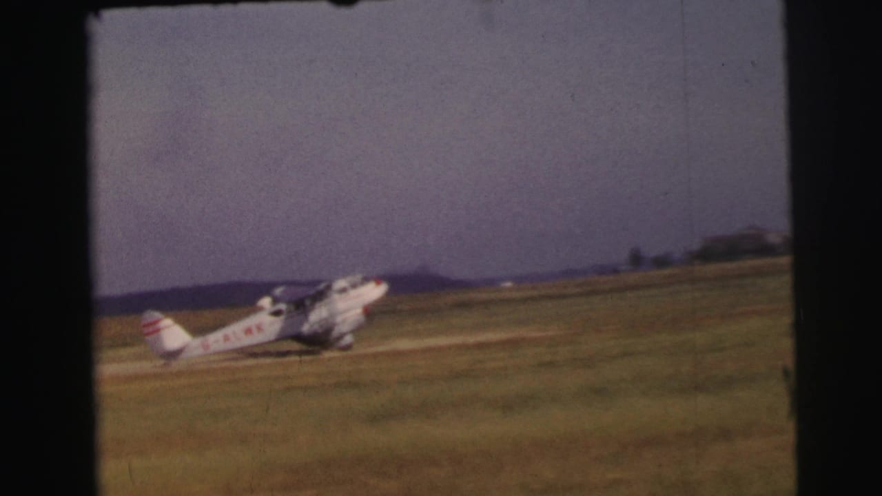 The aircraft continues taxiing across the open grass runway, with red registration markings visible on the fuselage.