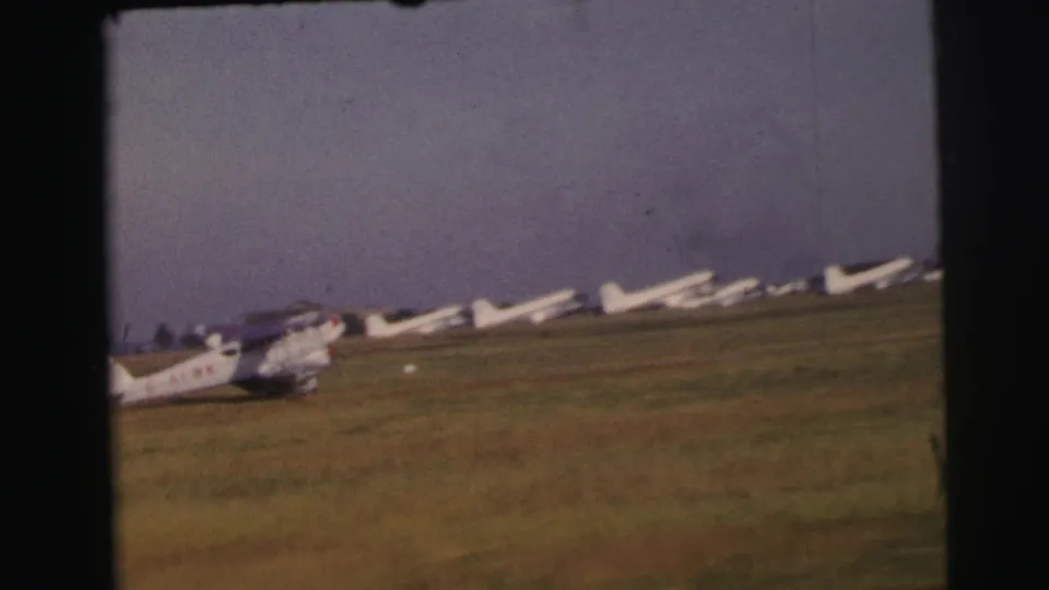 A small marked aircraft taxis past parked white gliders or light aircraft on the grass airfield at Le Mans, based on the clip metadata.