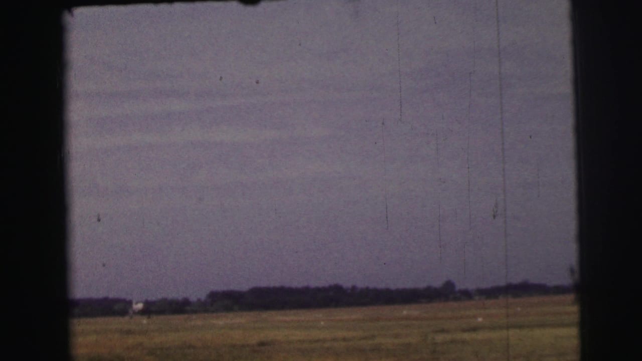 Flat meadow under a muted sky seen through dark film or window borders.