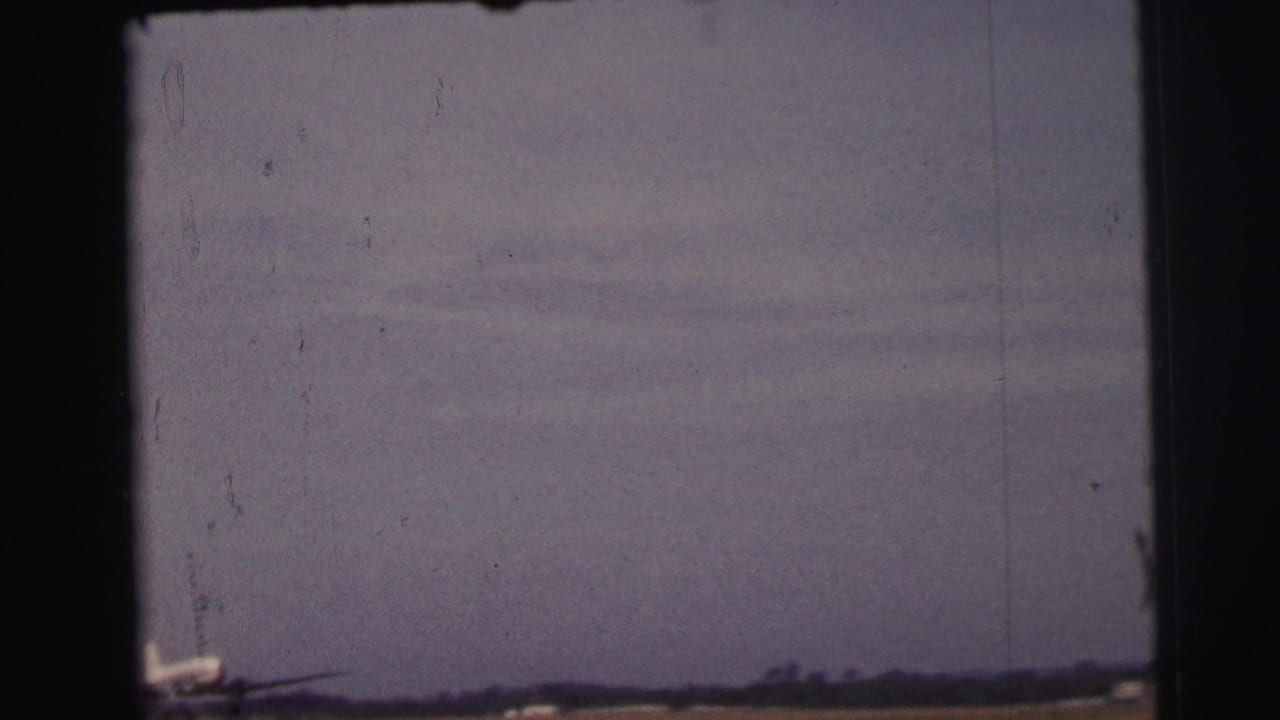 1954 Le Mans 8mm frame showing a hazy airfield horizon and the partial nose of a small propeller airplane at the lower left.
