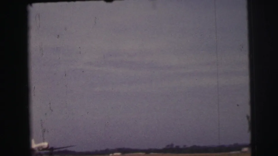 1954 Le Mans 8mm frame showing a hazy airfield horizon and the partial nose of a small propeller airplane at the lower left.