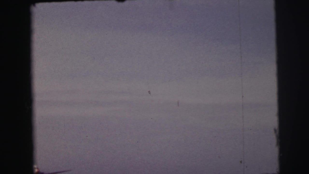 1954 Le Mans 8mm frame with the aircraft barely visible near the horizon under a muted, overcast sky.