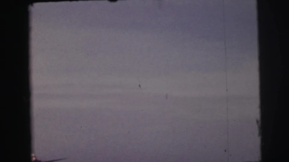 1954 Le Mans 8mm frame with the aircraft barely visible near the horizon under a muted, overcast sky.