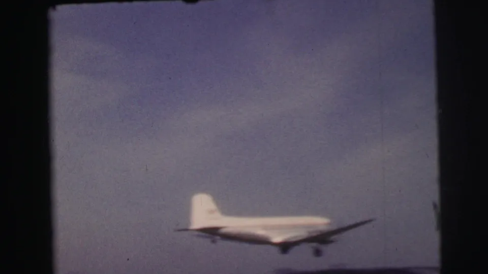 1954 8mm footage from Le Mans, France, showing a small propeller airplane lifting into a pale sky above an open field.