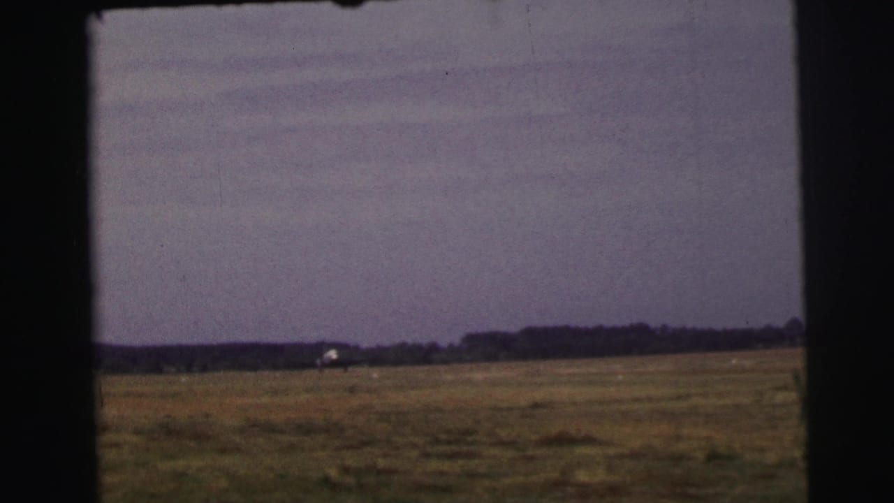 Le Mans, France, 1954 home-movie frame of a small airplane far across a broad grass field under a hazy sky.