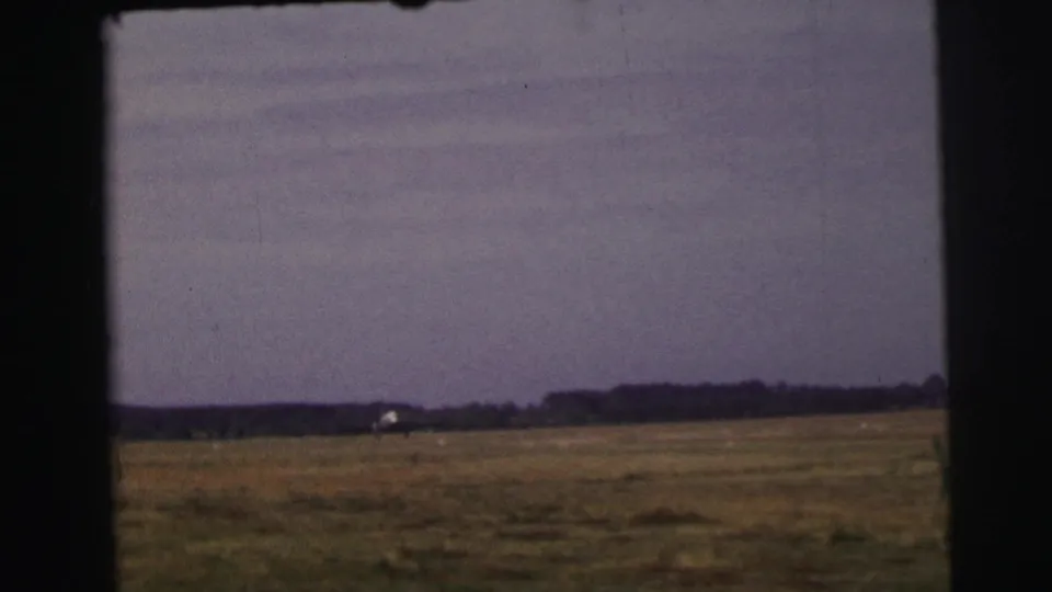 Le Mans, France, 1954 home-movie frame of a small airplane far across a broad grass field under a hazy sky.