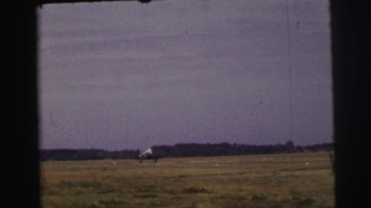 Small propeller airplane on a distant grass runway under a pale sky.