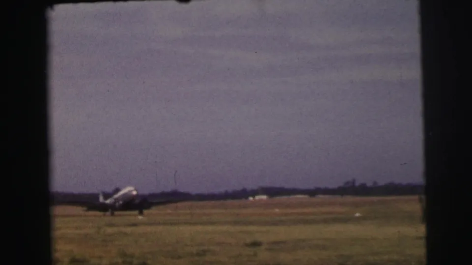 The plane remains on the grass runway near the end of the Le Mans home-movie clip, with dark frame borders and a low horizon visible.