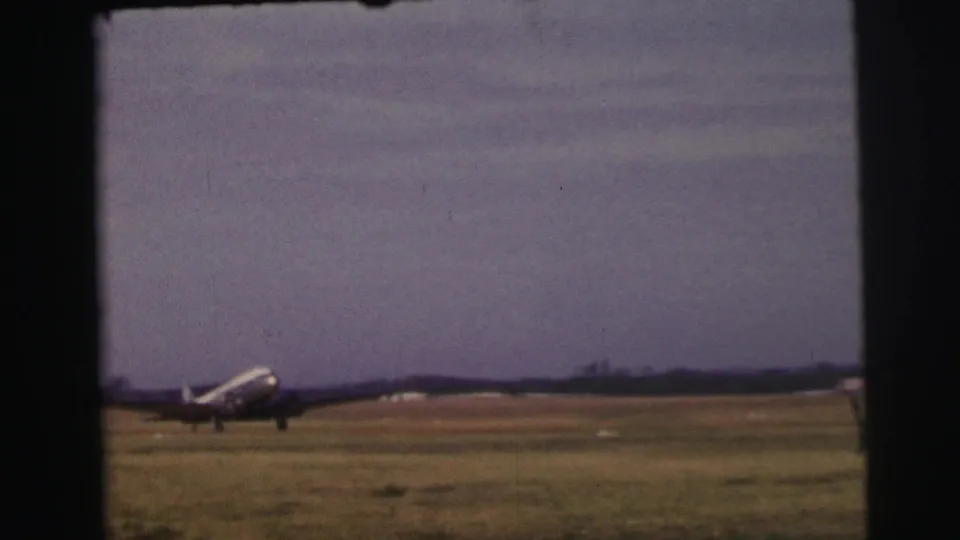 A propeller passenger plane appears at distance on a grassy Le Mans airfield in 1954, framed by dark 8mm film edges.