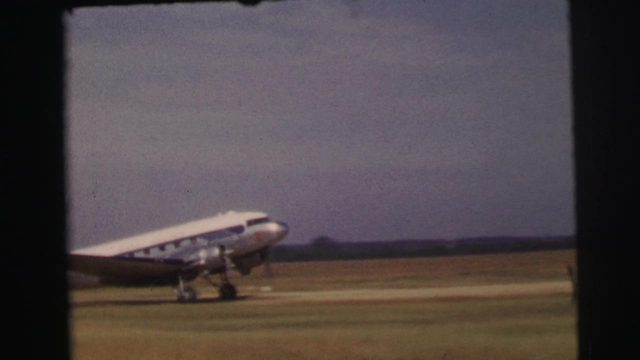 A silver-and-white propeller aircraft rolls across a grassy runway at Le Mans, France, in 1954 home-movie footage.