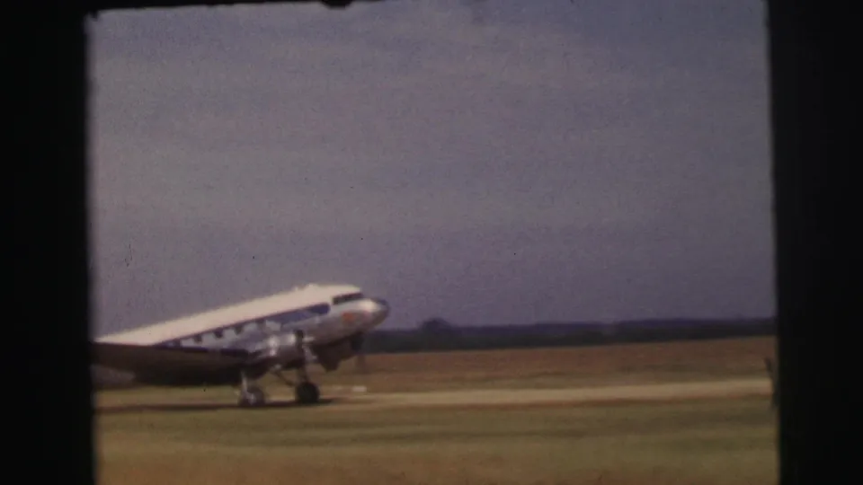 A silver-and-white propeller aircraft rolls across a grassy runway at Le Mans, France, in 1954 home-movie footage.
