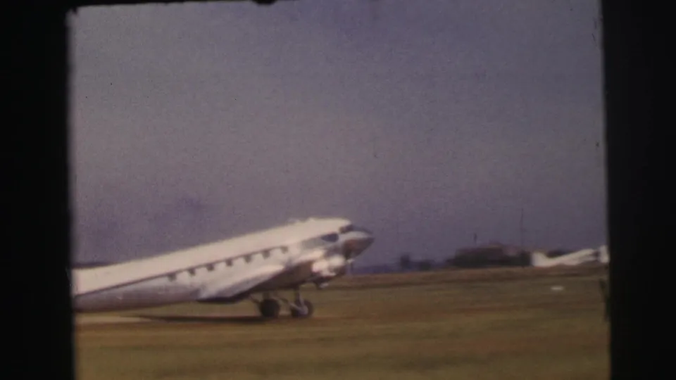 A closer home-movie view shows the aircraft nose, cabin windows, and landing gear as it passes across the grassy runway.