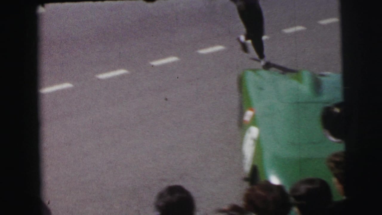 1954 Le Mans 8mm frame with a green open race car partly obscured by spectators and film gate edges.