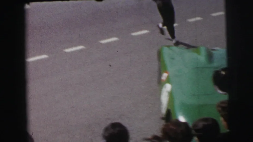 1954 Le Mans 8mm frame with a green open race car partly obscured by spectators and film gate edges.