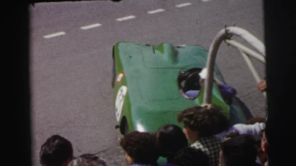 Le Mans 1954 frame with a green race car stopped or moving slowly as a helmeted person settles into the cockpit.