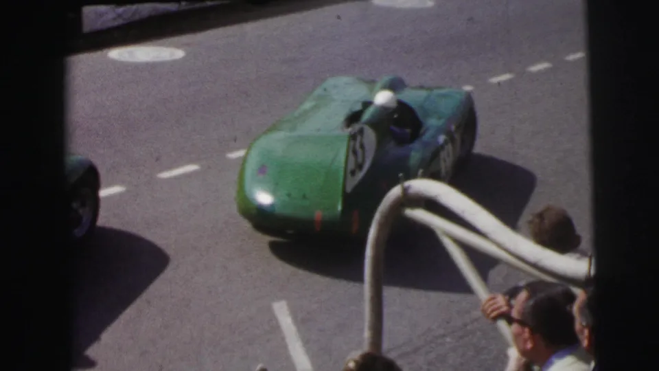 The green number 23 open-cockpit car moves along the Le Mans track in 1954, filmed from a spectator viewpoint.