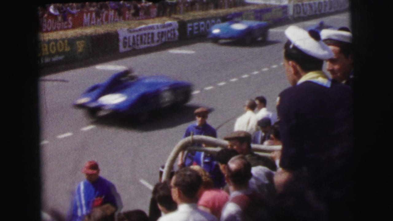 At Le Mans in 1954, a blue sports car blurs past spectators watching from beside the racing circuit.